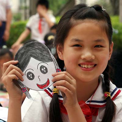 A young, smiling Asian girl with her drawn smiling-faced self-portrait